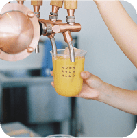 カンキツスタンドオレンジと書かれたコップにオレンジジュースを注いでいる写真